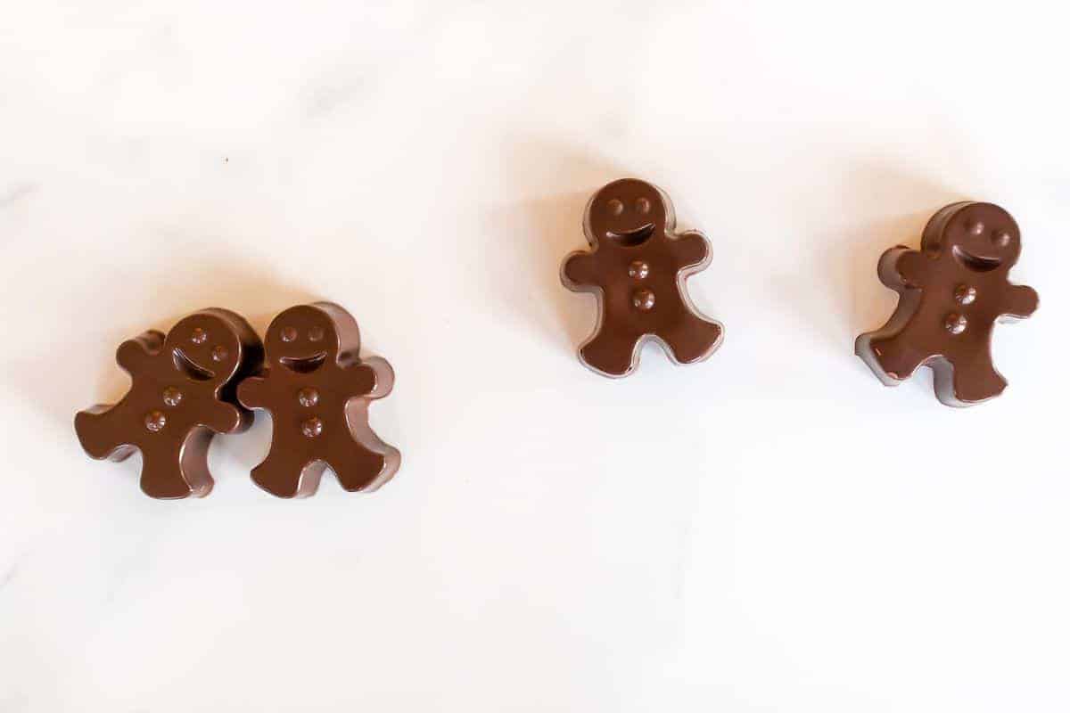 A group of dark chocolate hot chocolate bombs shaped as gingerbread men on a white marble surface.