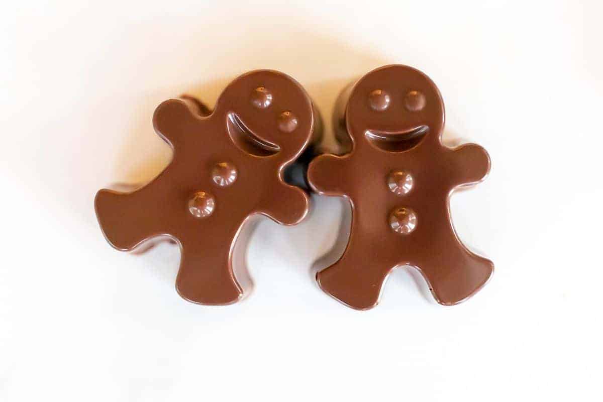 A pair of dark chocolate hot chocolate bombs shaped as gingerbread men on a white marble surface.