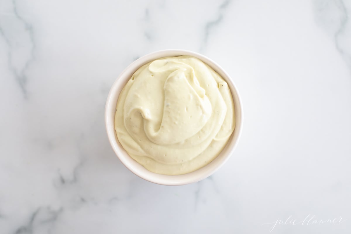 A white ramekin full of homemade avocado mayo, on a marble countertop.