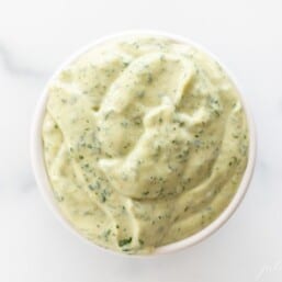 A white bowl full of cilantro aioli on a marble surface.