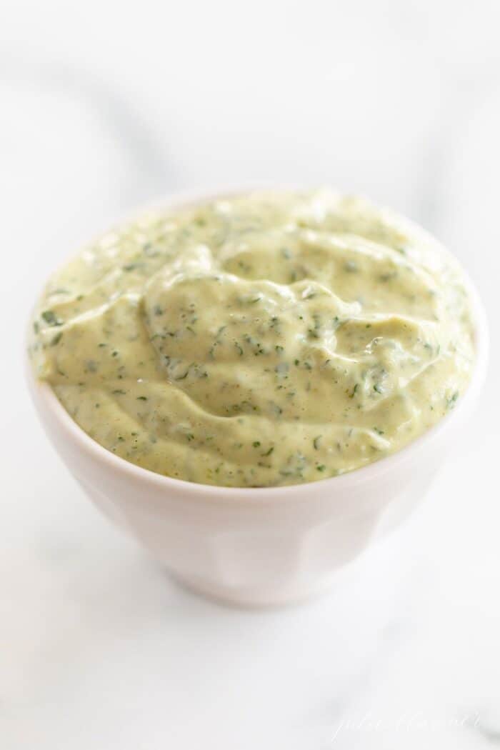 A white bowl full of cilantro aioli on a marble surface.