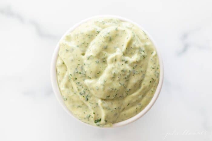 A white bowl full of cilantro aioli on a marble surface.