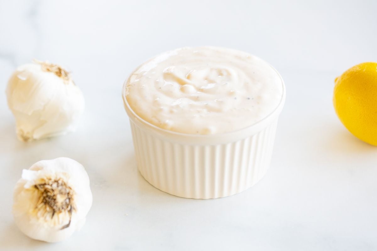 A small white bowl of garlic aioli with a garlic bulb to the side.