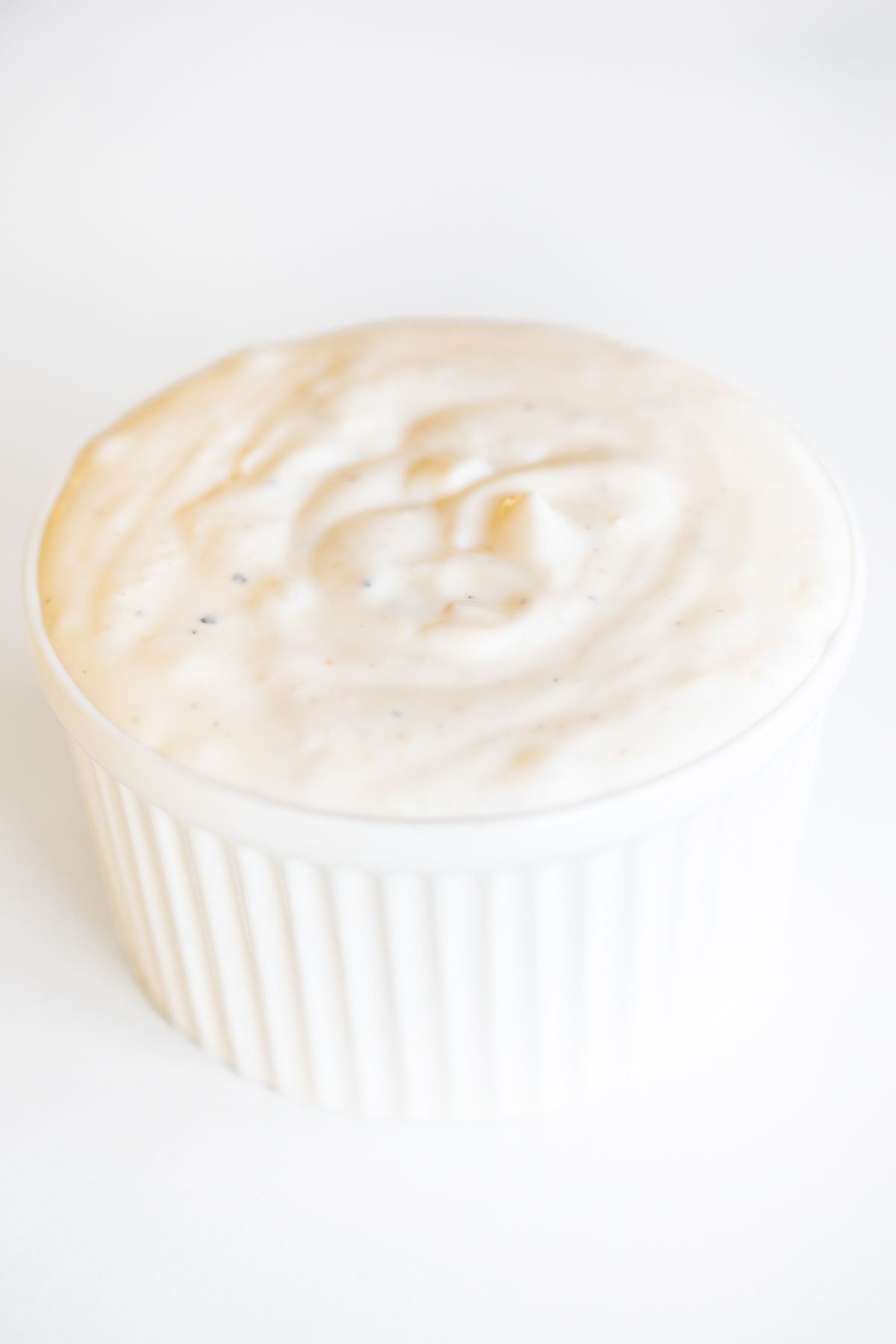 A white bowl of garlic aioli on a white countertop.