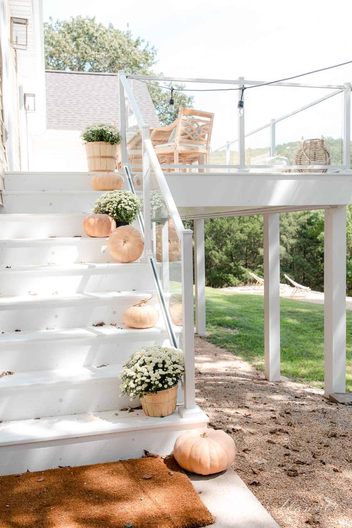 white deck with glass deck railing pumpkins mums and string lights