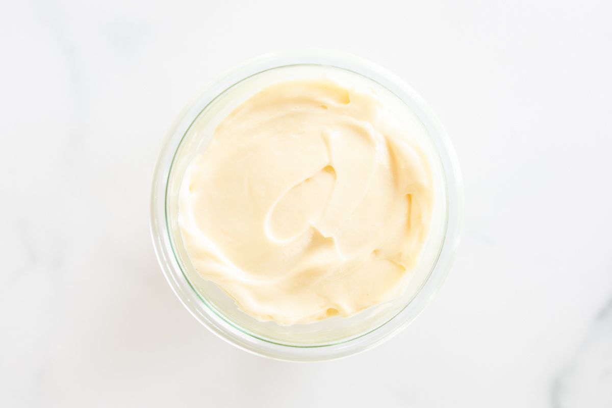 A small glass jar of mayonnaise for a tutorial on how to make mayo, it's resting on a marble countertop.