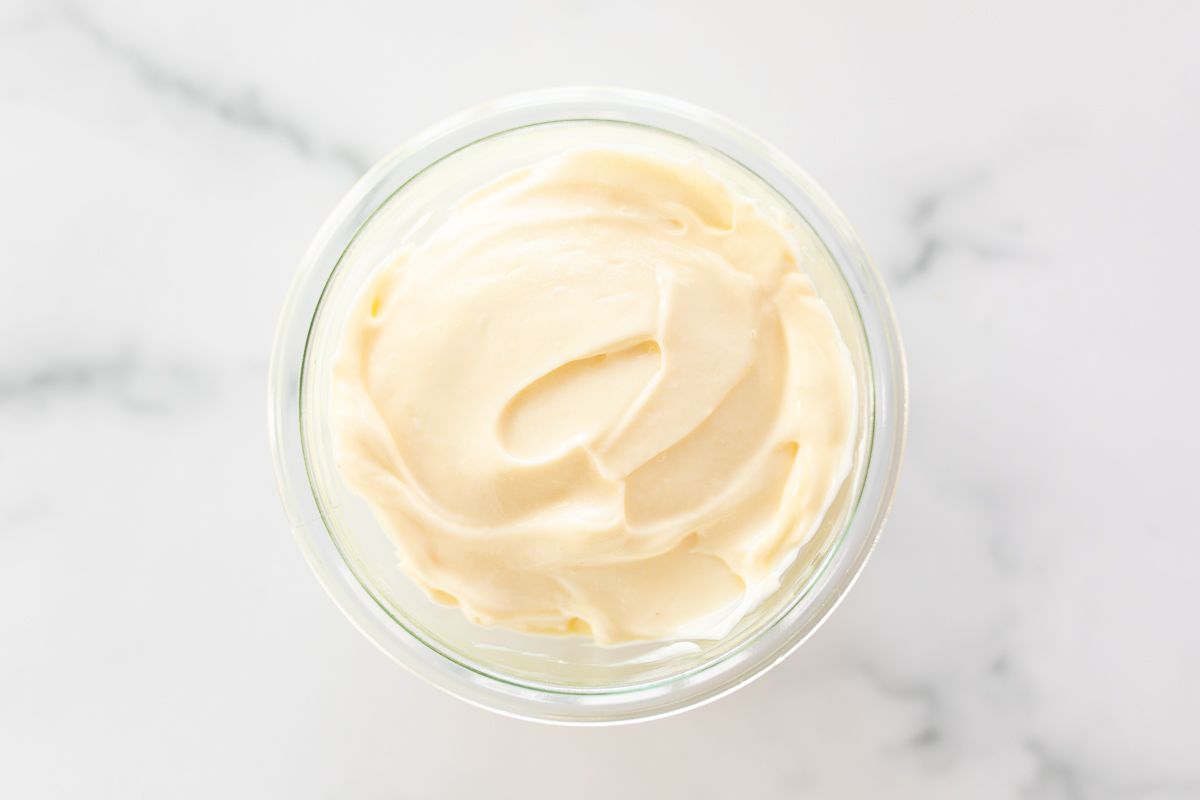 A small glass jar of mayonnaise for a tutorial on how to make mayo, it's resting on a marble countertop.