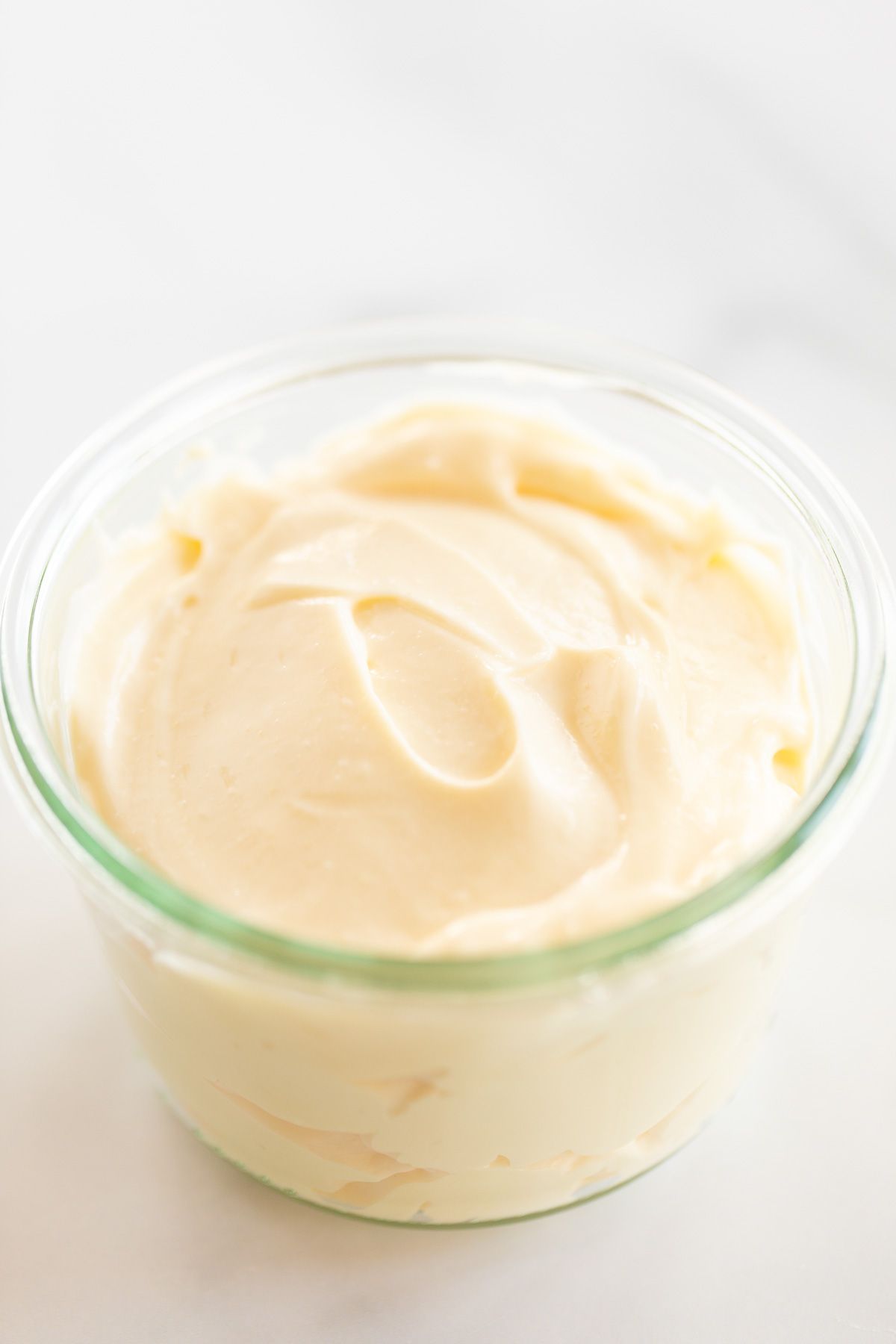 A small glass jar of mayonnaise for a tutorial on how to make mayo, it's resting on a marble countertop.