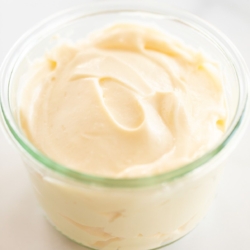 A small glass jar of mayonnaise for a tutorial on how to make mayo, it's resting on a marble countertop.