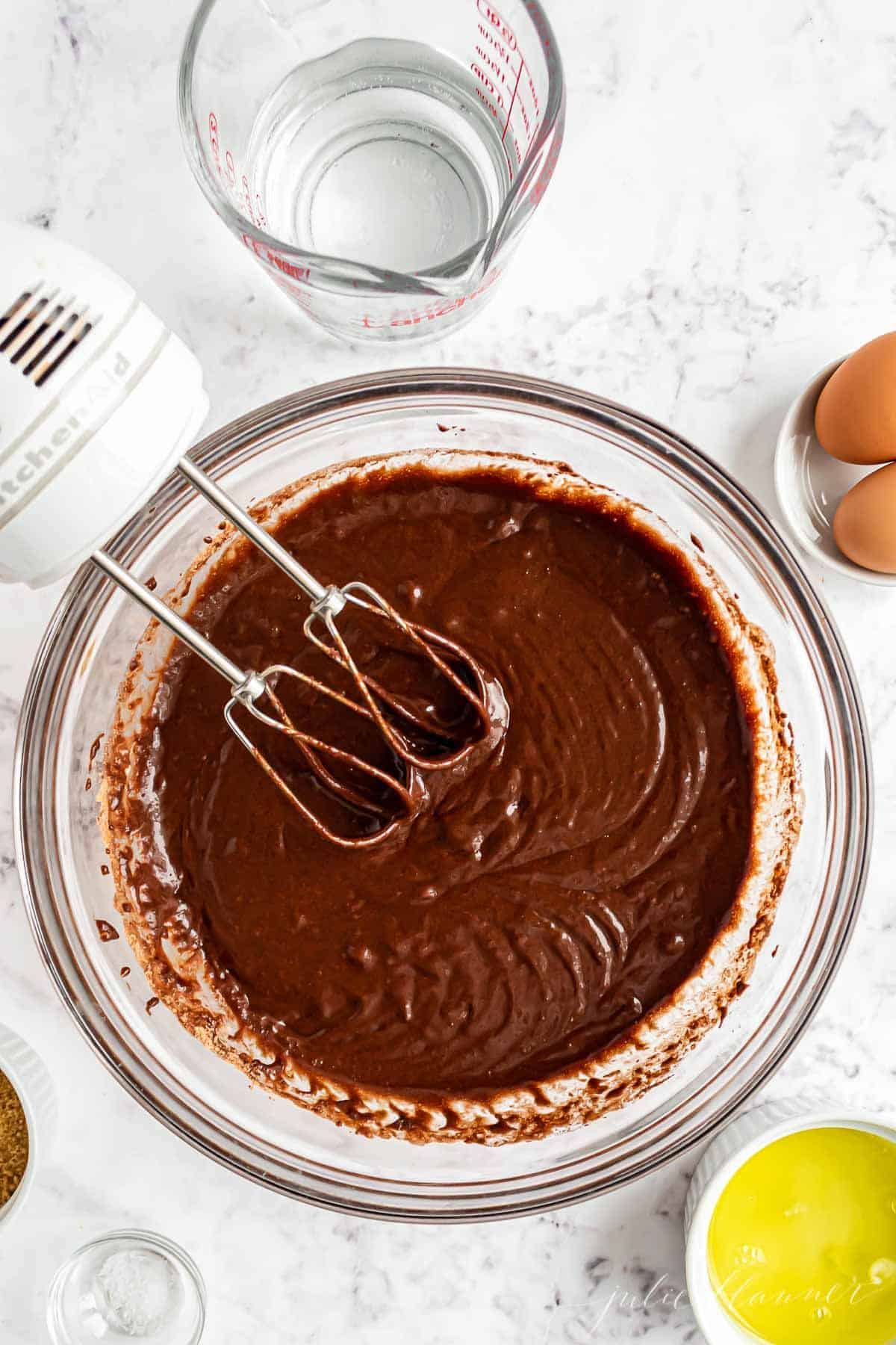 Chocolate cupcake batter in a clear glass bowl, ingredients for smores cupcakes surrounding.