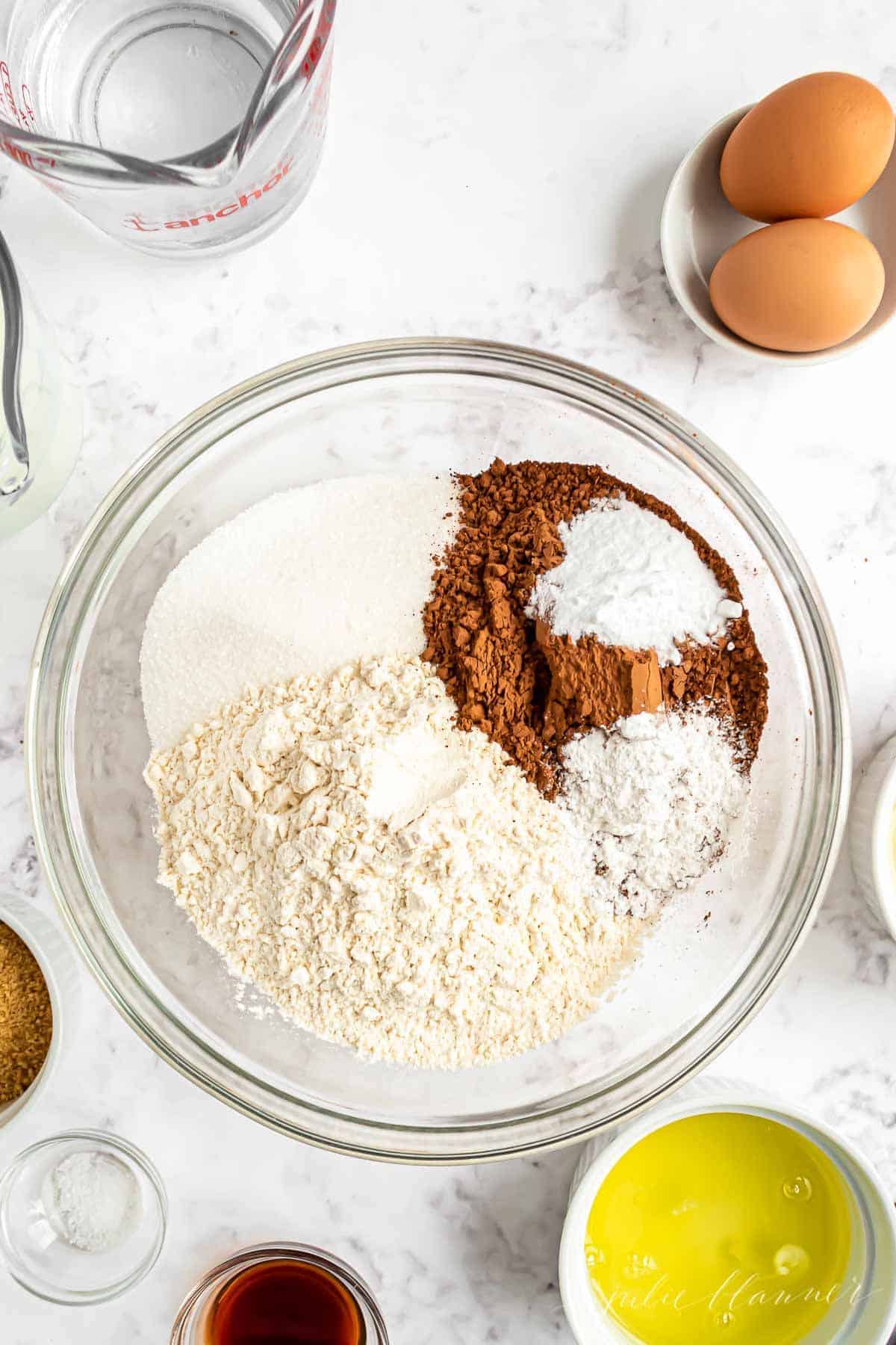 Dry ingredients for smores cupcake recipe in a clear glass bowl on a marble countertop.