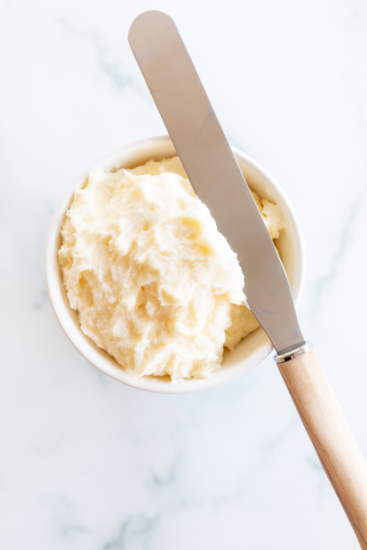 A bowl of whipped butter with a wooden-handled spreader on a marble surface, evoking the rich, homemade goodness found in Amish sugar cookies.