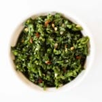 A white ramekin full of chimichurri on a marble surface.