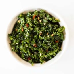 A white ramekin full of chimichurri on a marble surface.