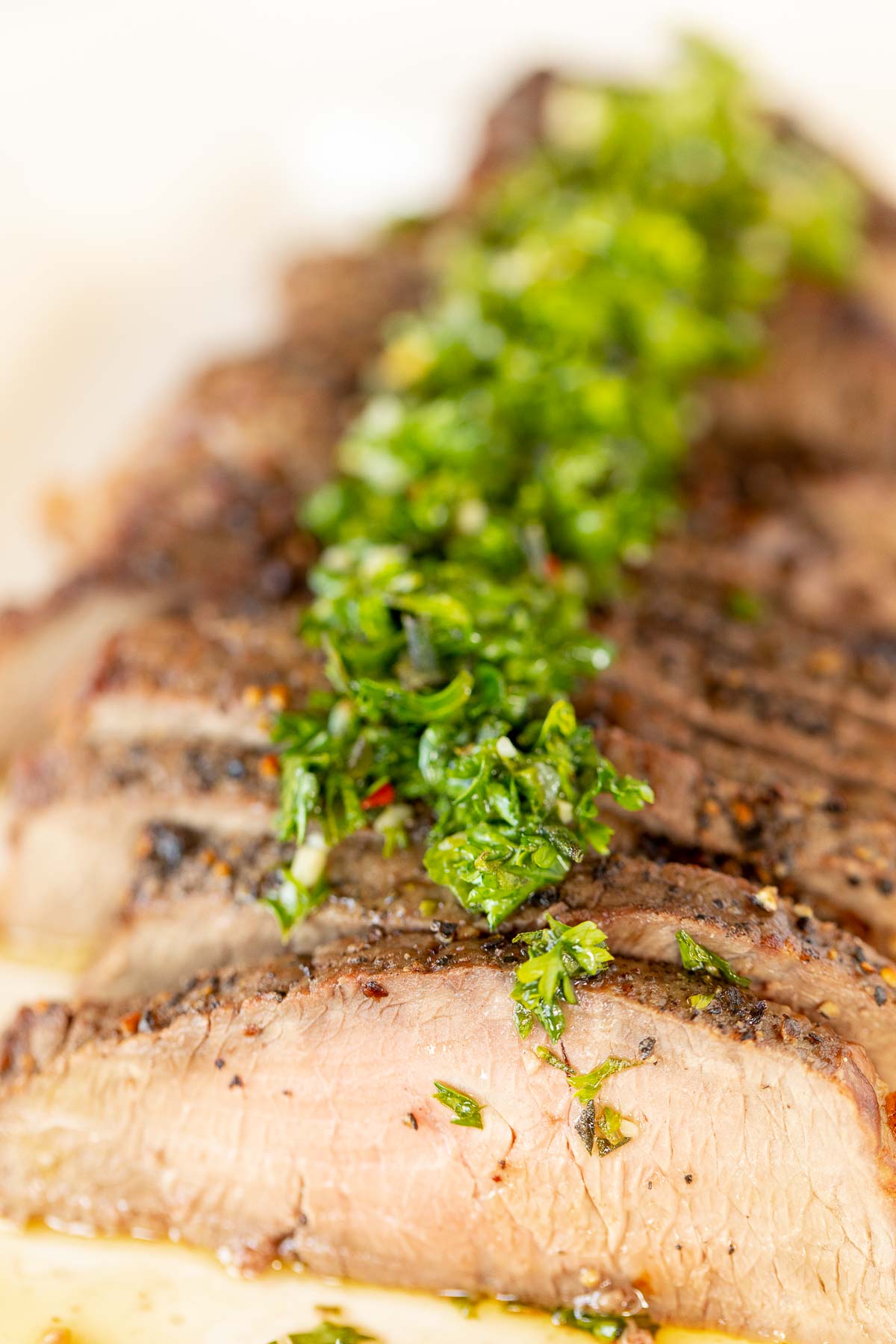 Sliced steak on a white plate, topped with chimichurri.