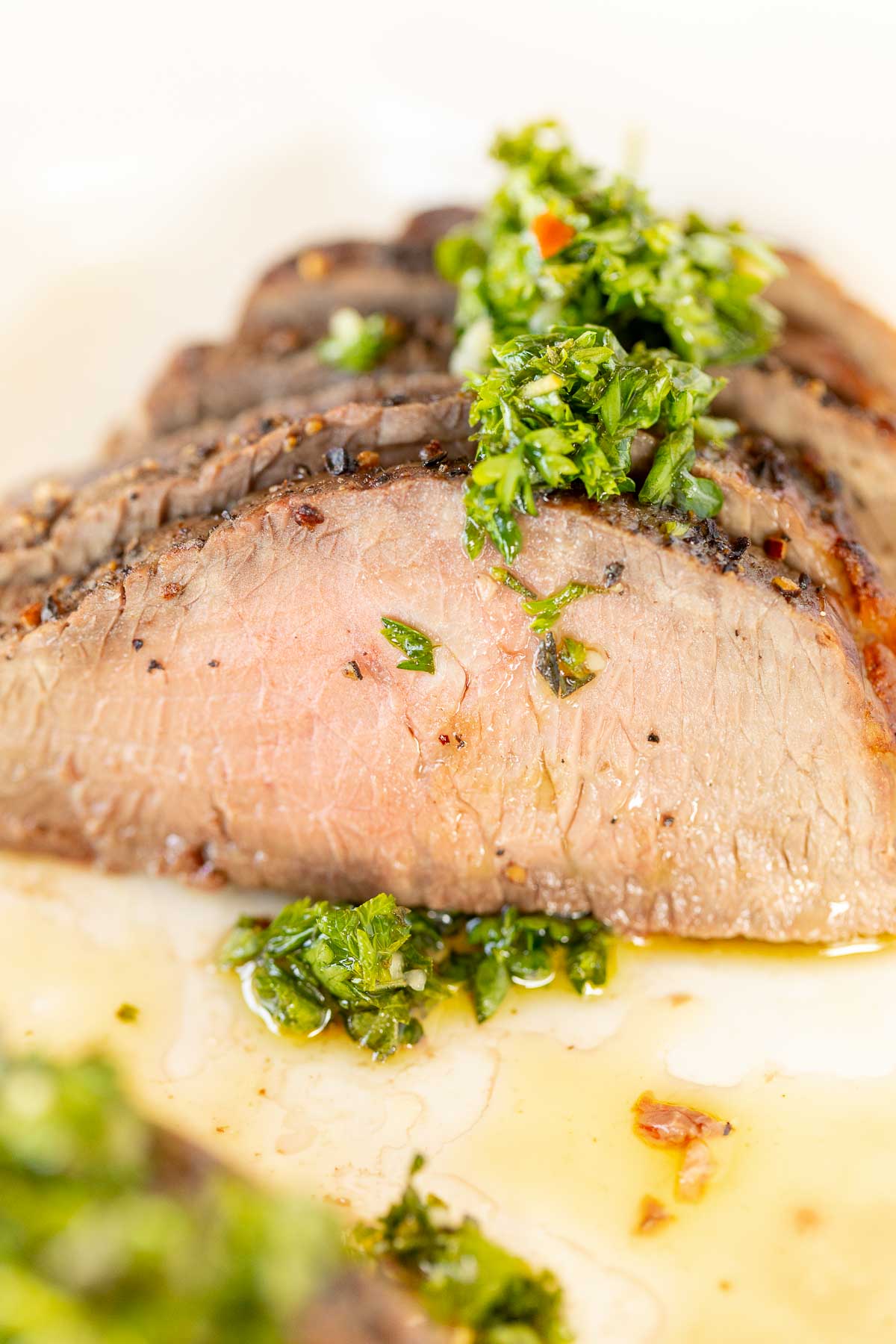 Sliced steak on a white plate, topped with chimichurri.