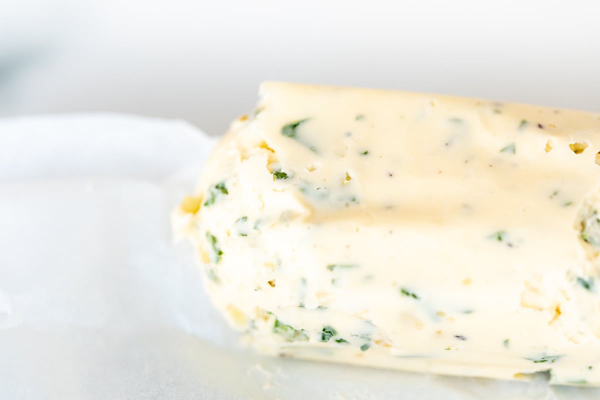 A roll of herbed steak butter on a white surface.