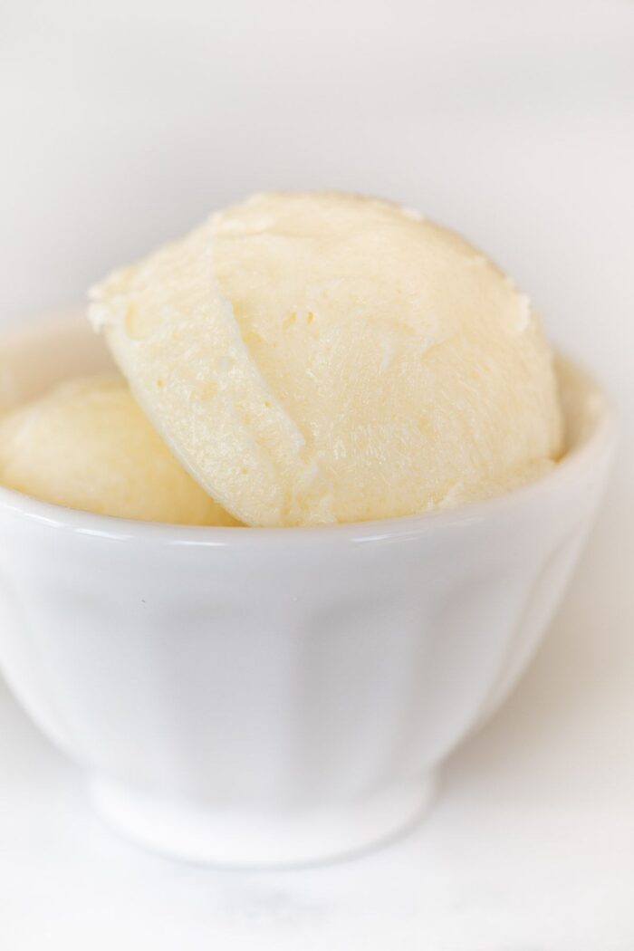 A small white bowl full of flavored butter on a marble counter top.