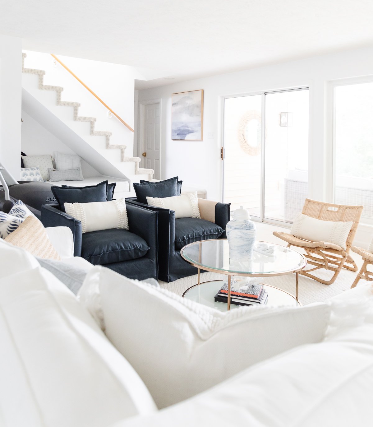 A white living room with a wall of windows, two navy blue chairs and a white sectional sofa.