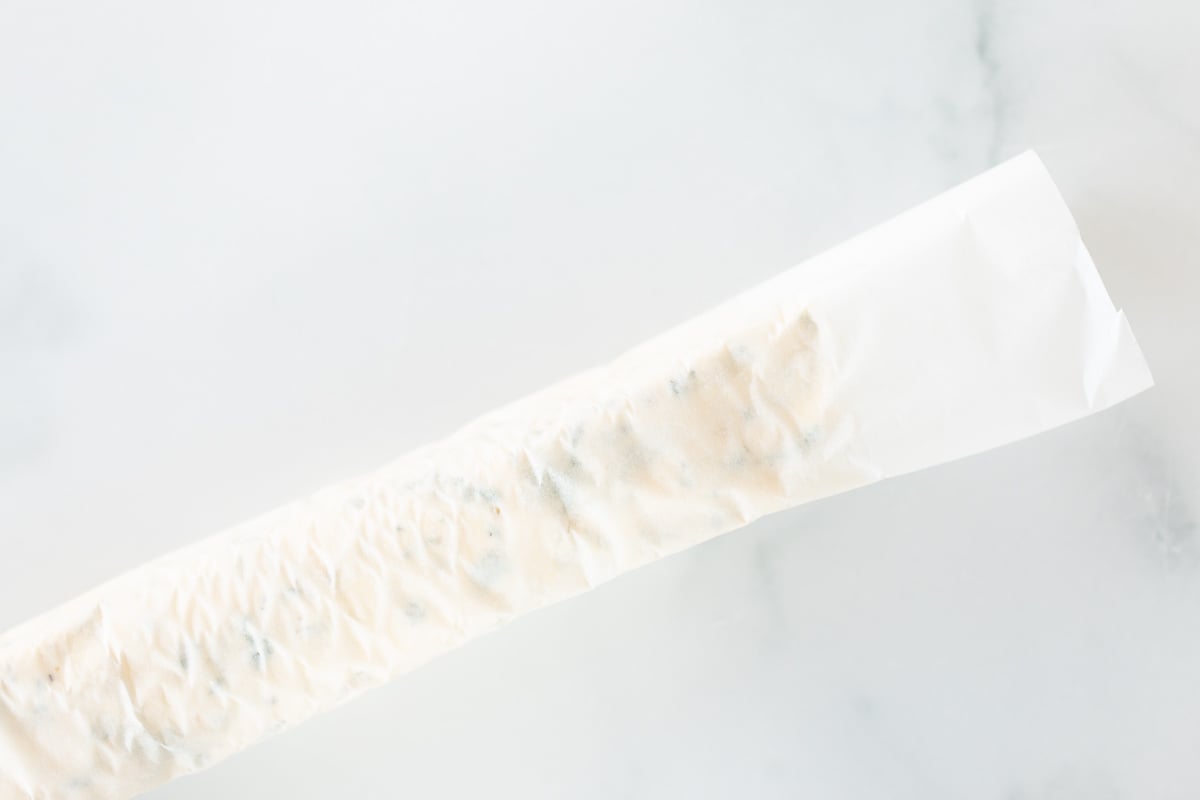 A roll of herbed steak butter on a white surface.