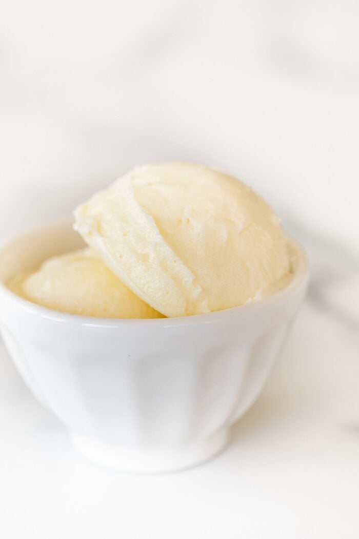 A small white bowl full of sweet butter on a marble counter top.