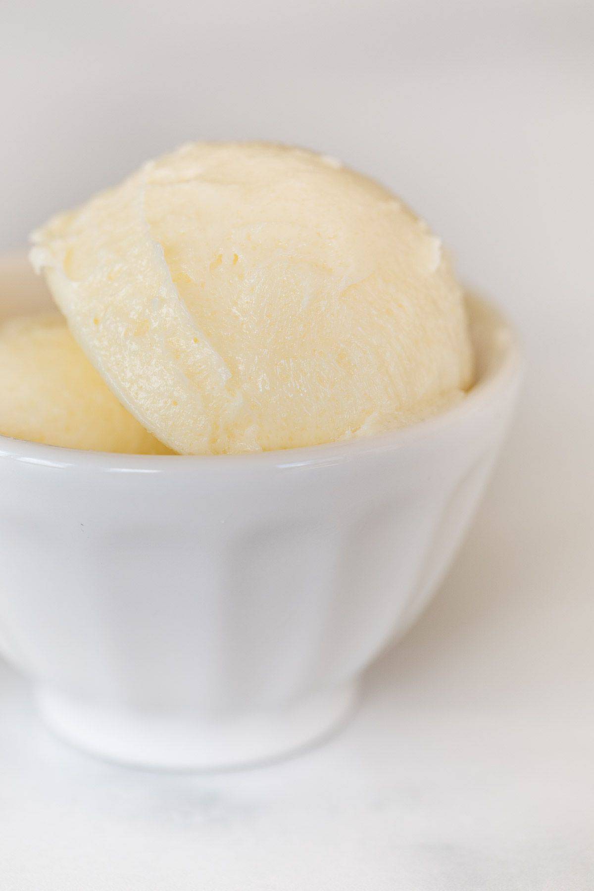 A small white bowl full of flavored butter on a marble counter top.