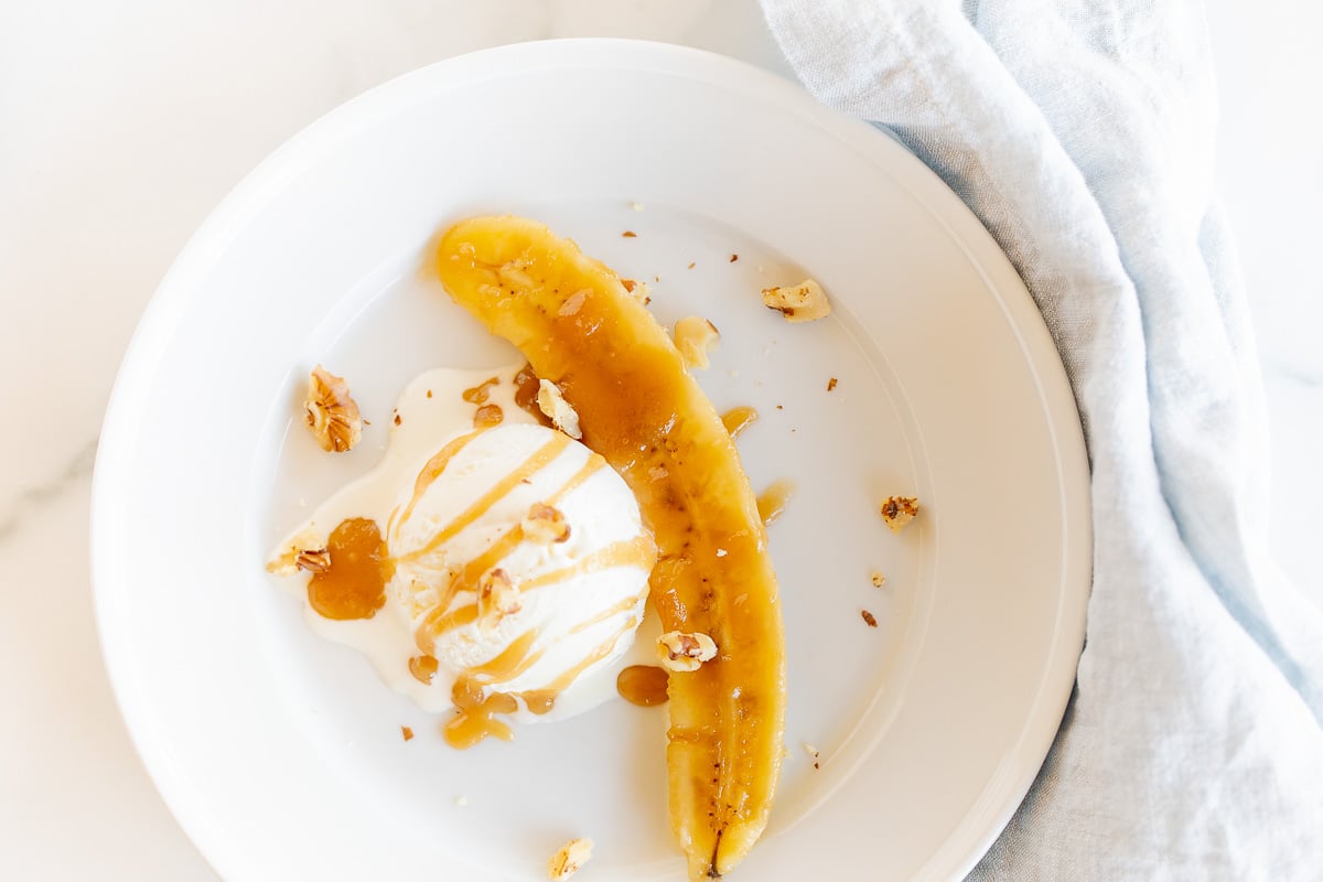 A white plate with ice cream and a banana slice drizzled in bananas foster sauce.