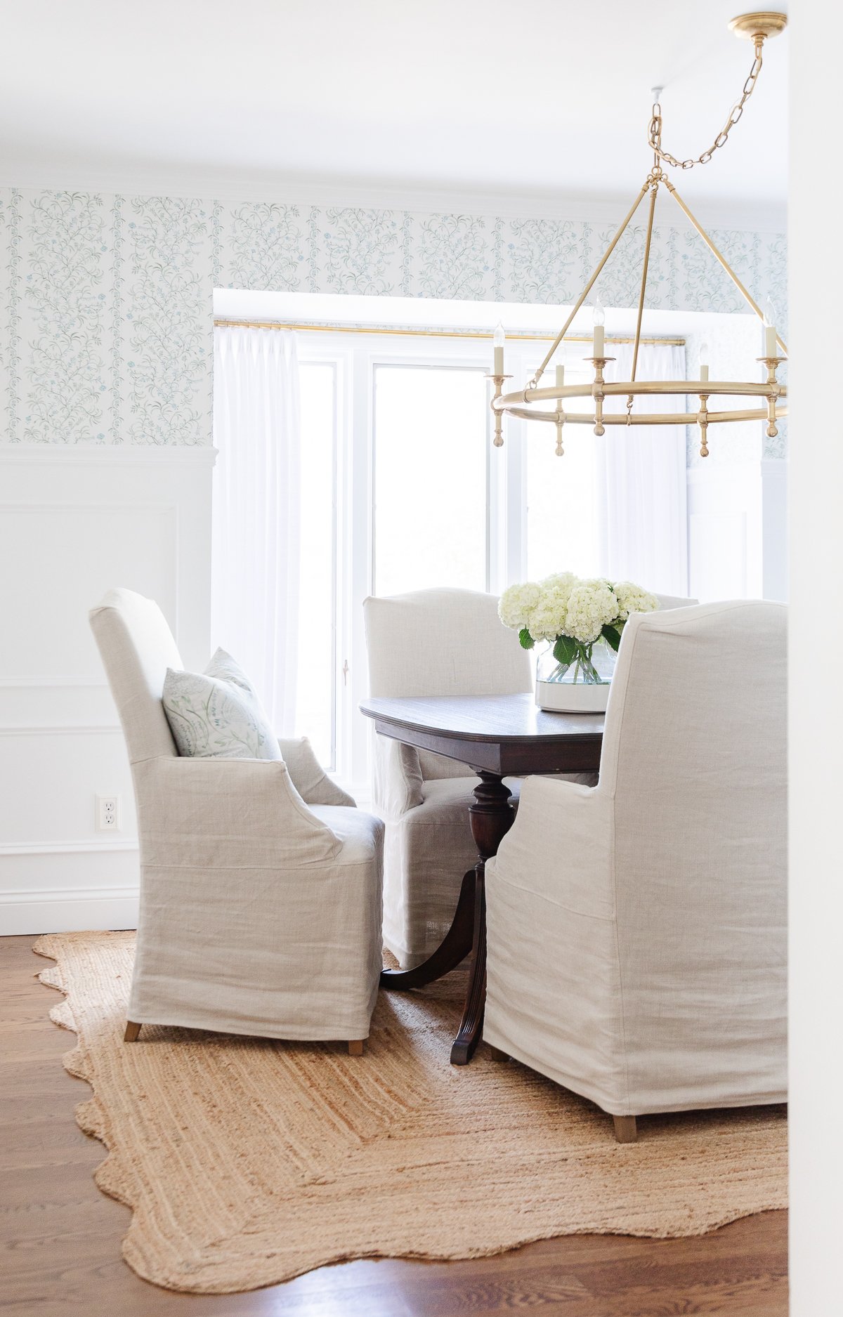 Elegant dining area with white upholstered chairs, a wooden table, a chandelier above, and decorative wallpaper accented by the best paint for trim.