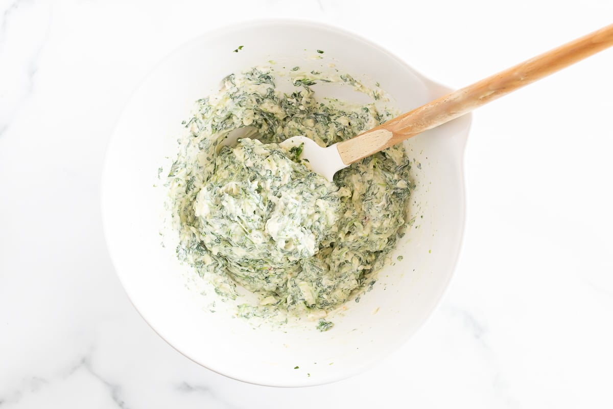 Cream cheese spinach dip in a white bowl with a wooden spoon.