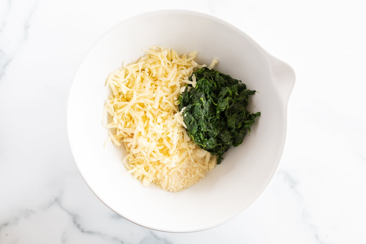 A white bowl with spinach dip containing cream cheese