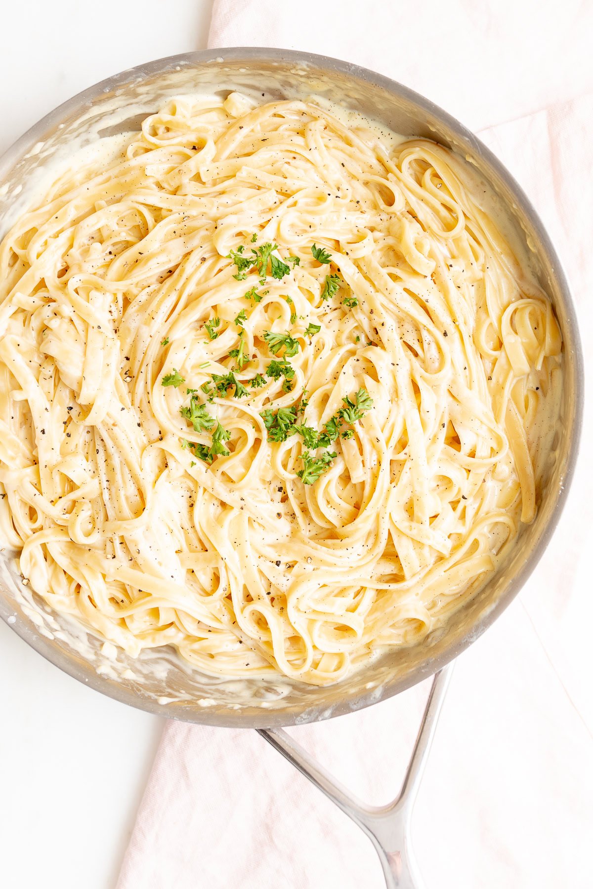 A skillet filled with creamy fettuccine Alfredo, crafted from a classic fettuccine Alfredo recipe, garnished with chopped parsley and cracked black pepper.