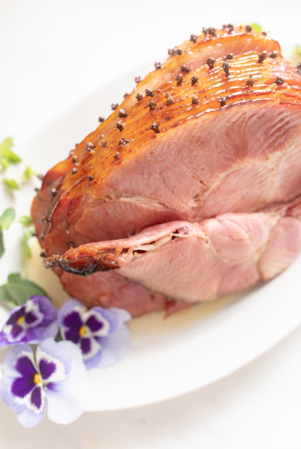 honey glazed ham garnished with fresh pansies on a white platter