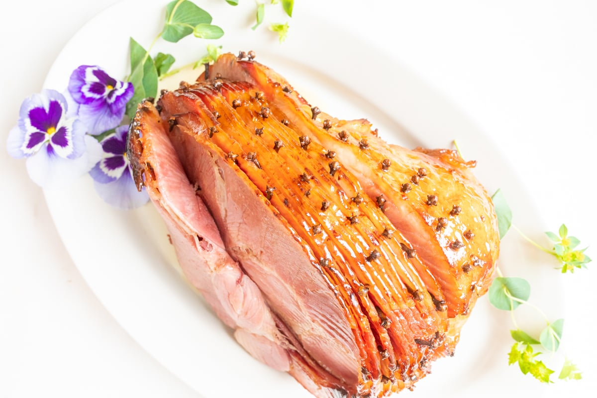 honey glazed ham garnished with fresh pansies on a white platter