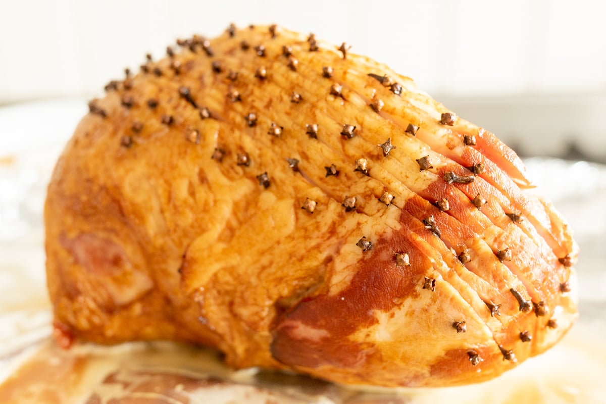 A sliced honey glazed ham on a white plate.