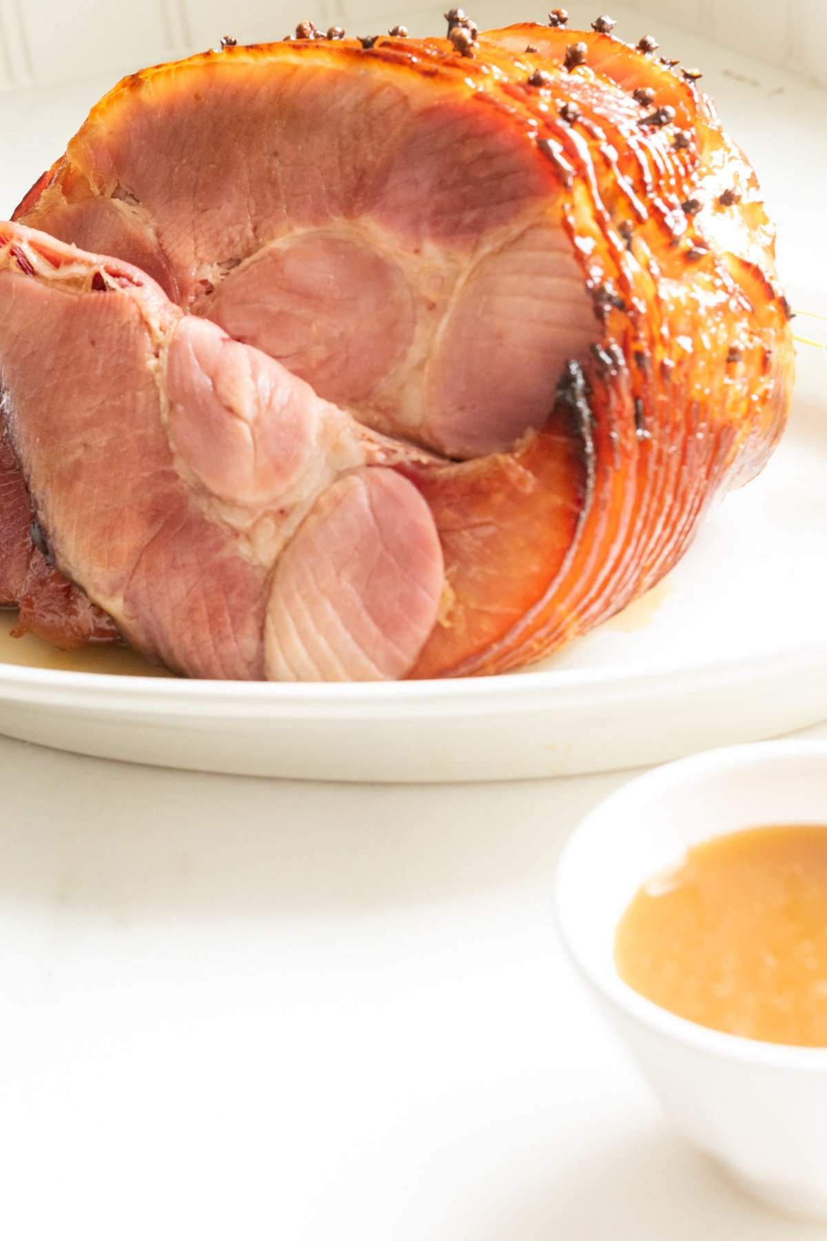 A sliced honey glazed ham on a white plate.