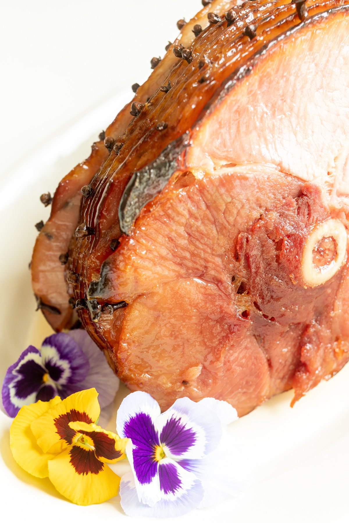 honey glazed ham garnished with fresh pansies on a white platter