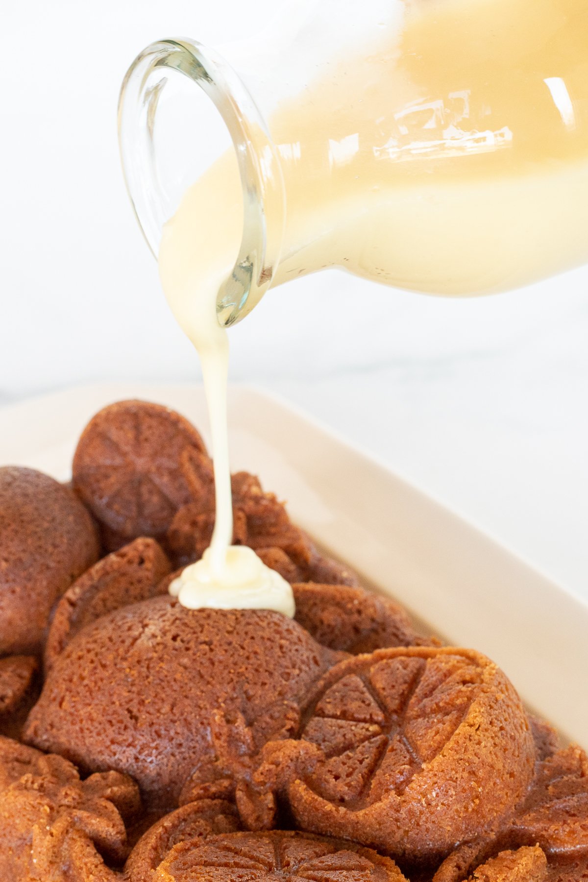 A glass bottle of orange glaze, pouring over an orange pound cake.