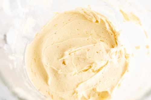 A close-up view of creamy orange pound cake batter in a mixing bowl.