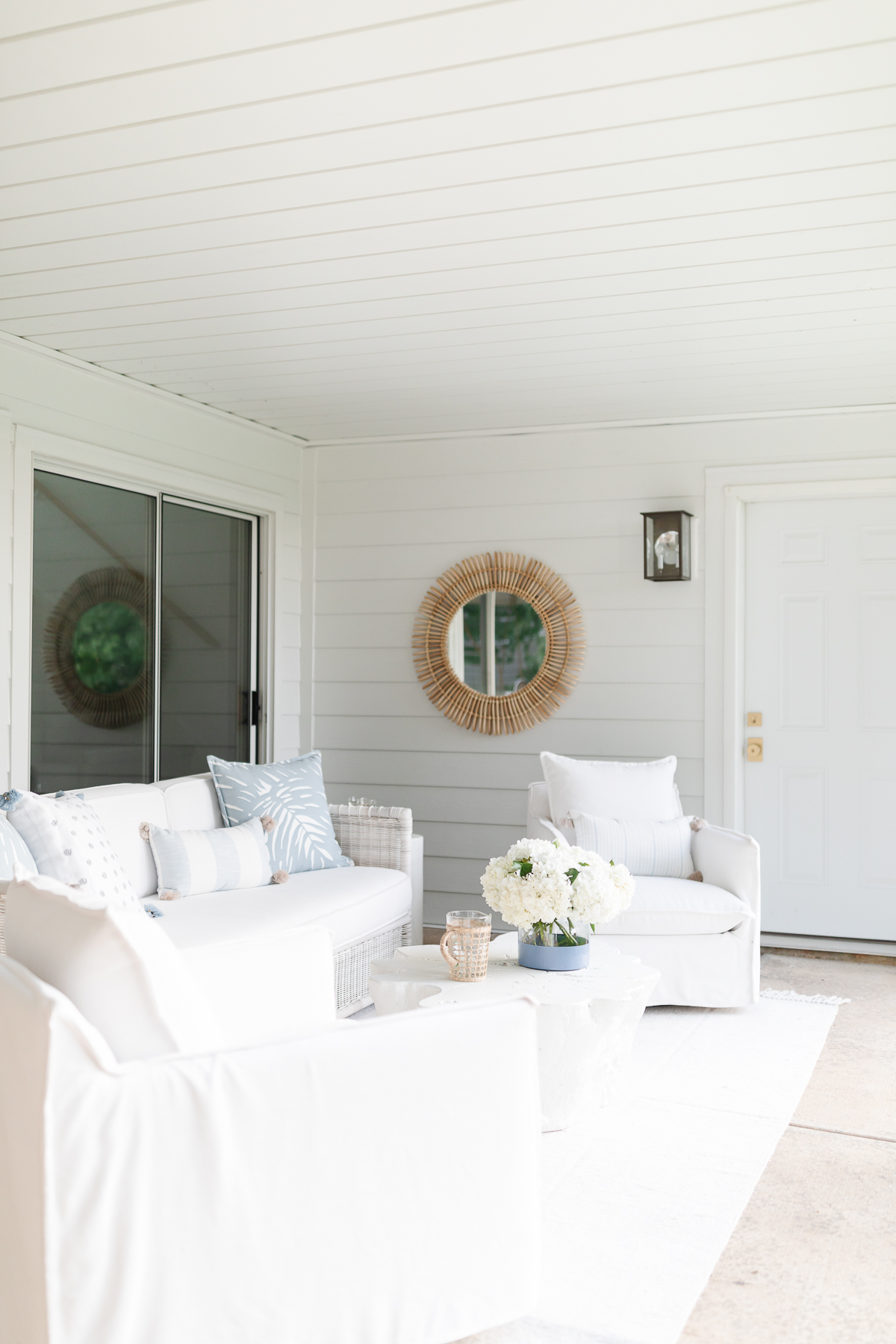 A white porch with white furniture and a mirror, with underdecking ceiling.