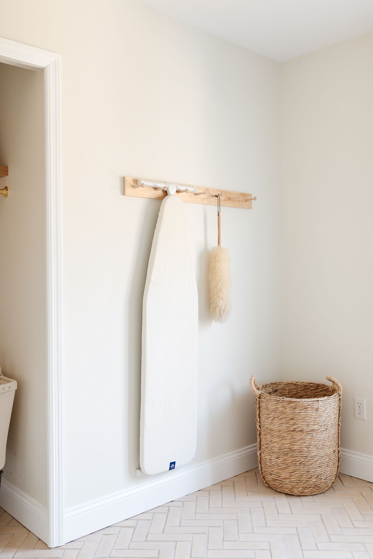 A peg rail on a white wall holding an ironing board and feather duster.