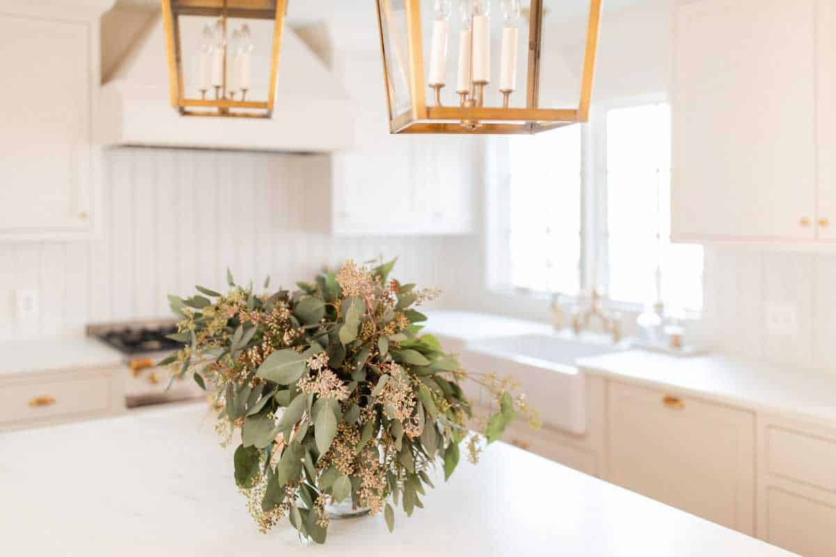 A cream kitchen with a vase of seeded eucalyptus on the island.