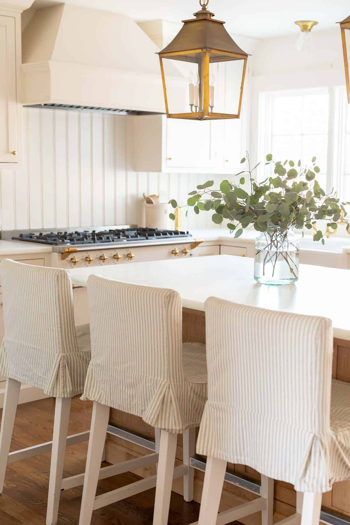 A clear glass vase on the island of a white kitchen, filled with silver dollar eucalyptus.