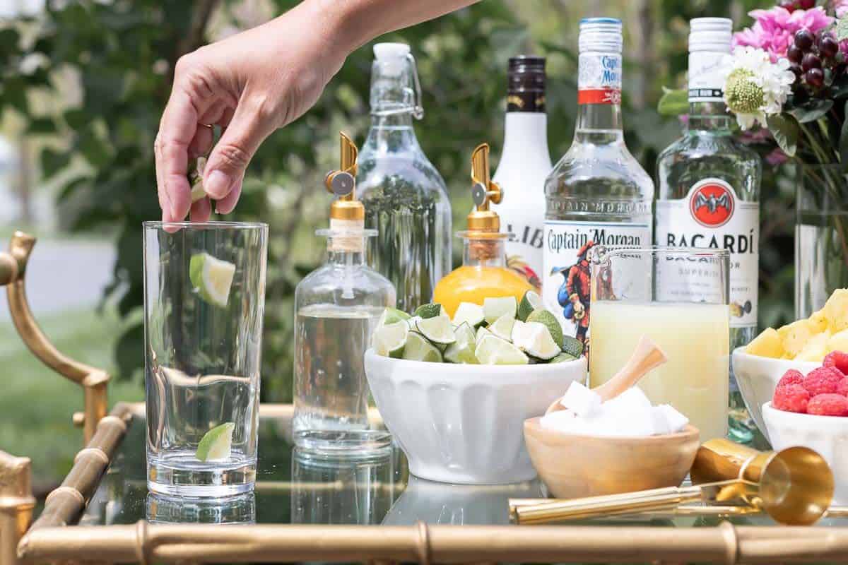 A hand reaching across a mojito bar to place limes in a glass.