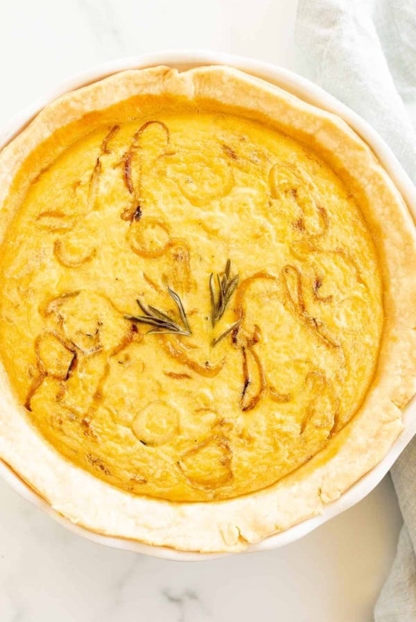 An onion quiche baked in a white pie pan on a marble surface.