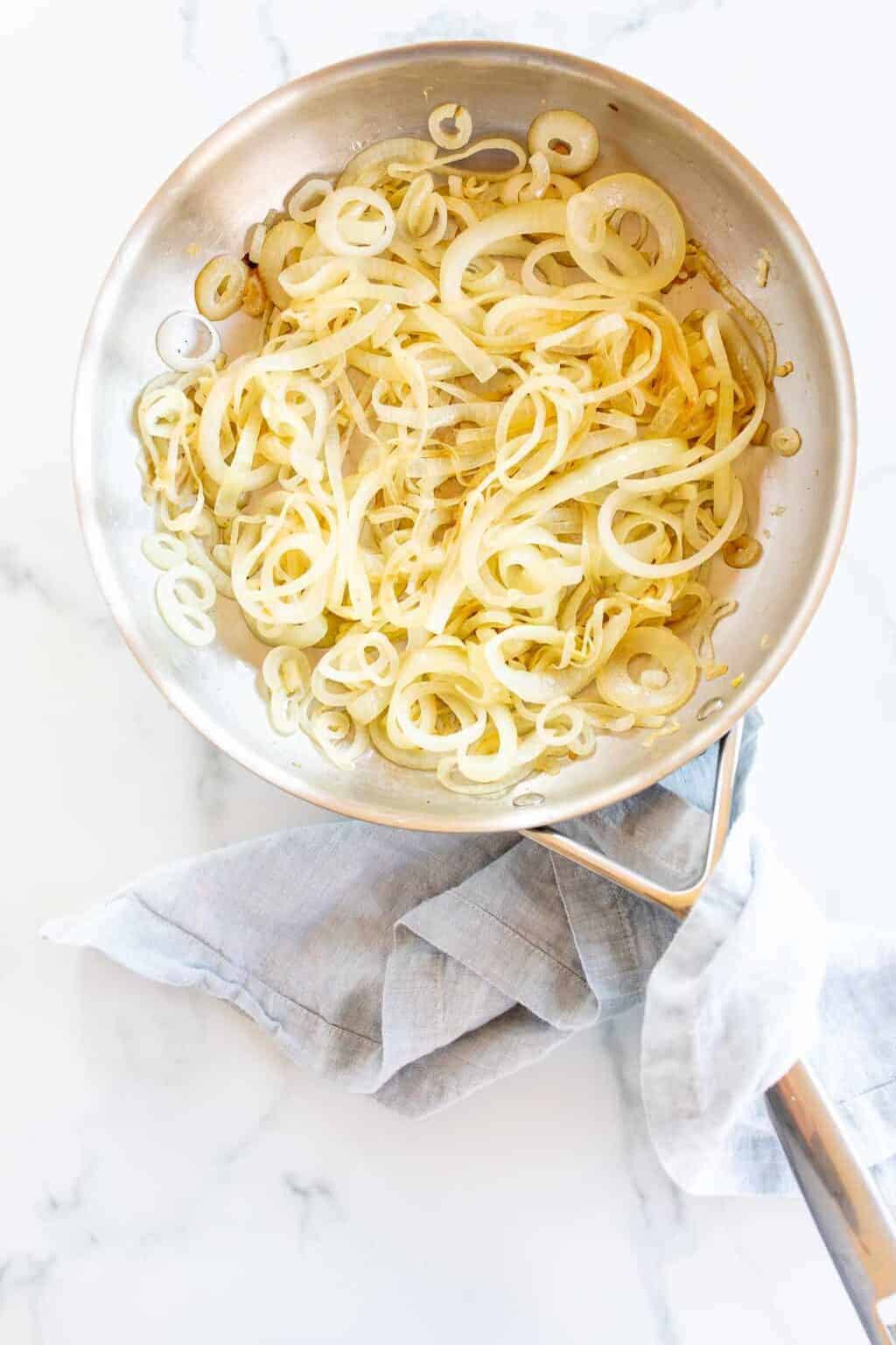 A frying pan on a marble surface filled with caramelized onions.