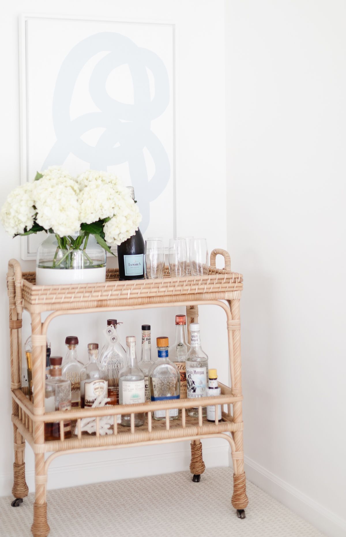 A rattan bar cart with modern blue and white art behind it