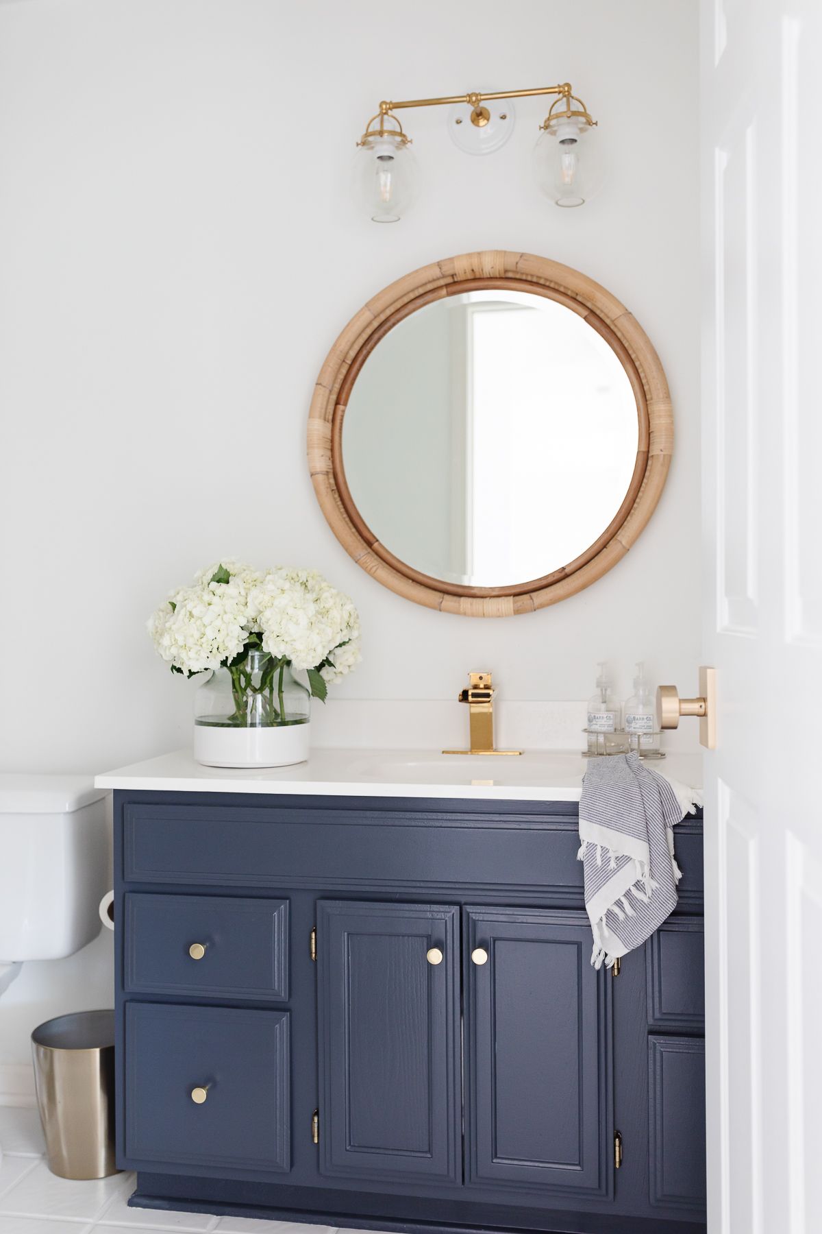 A modern coastal bath with a rattan mirror and a navy vanity