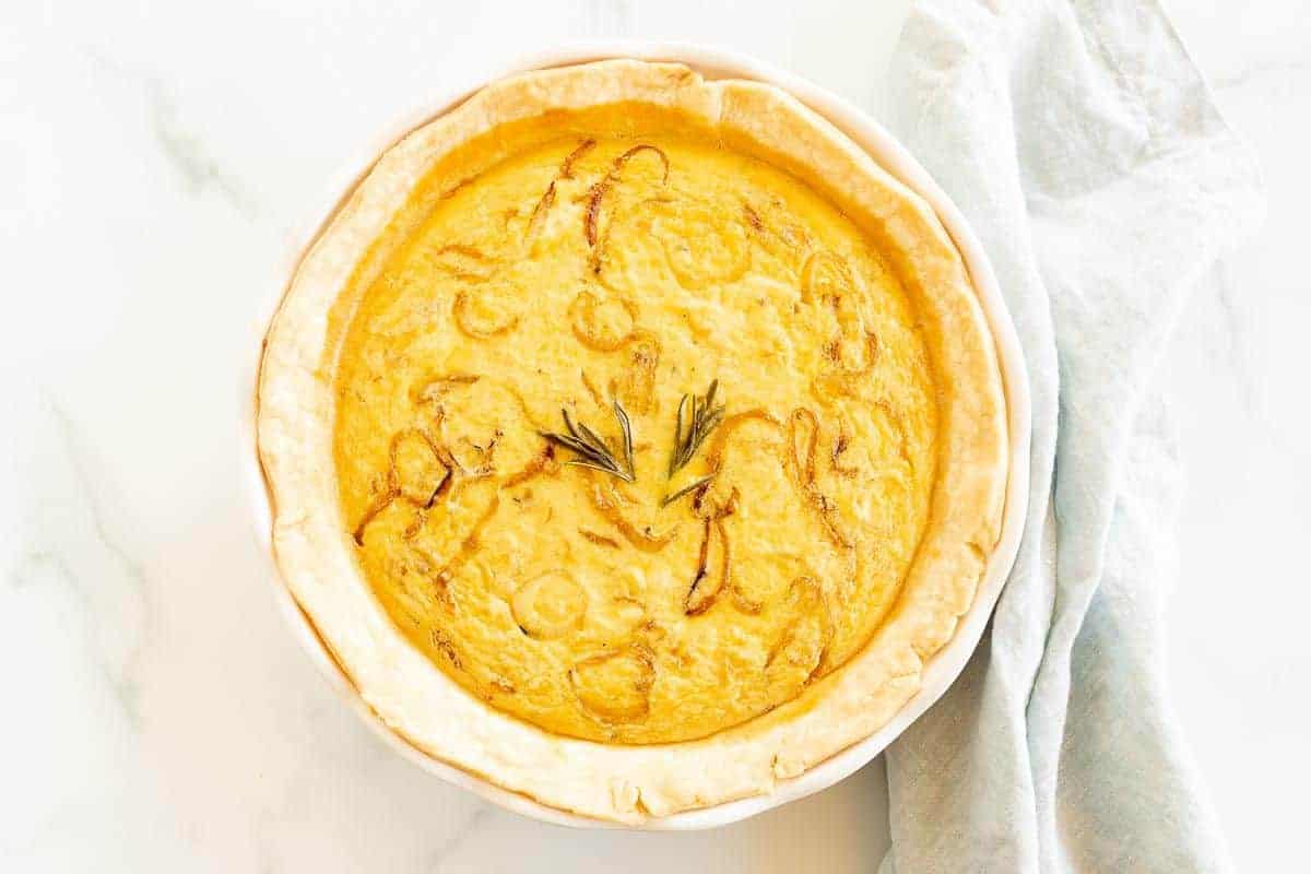 An onion quiche baked in a white pie pan on a marble surface.