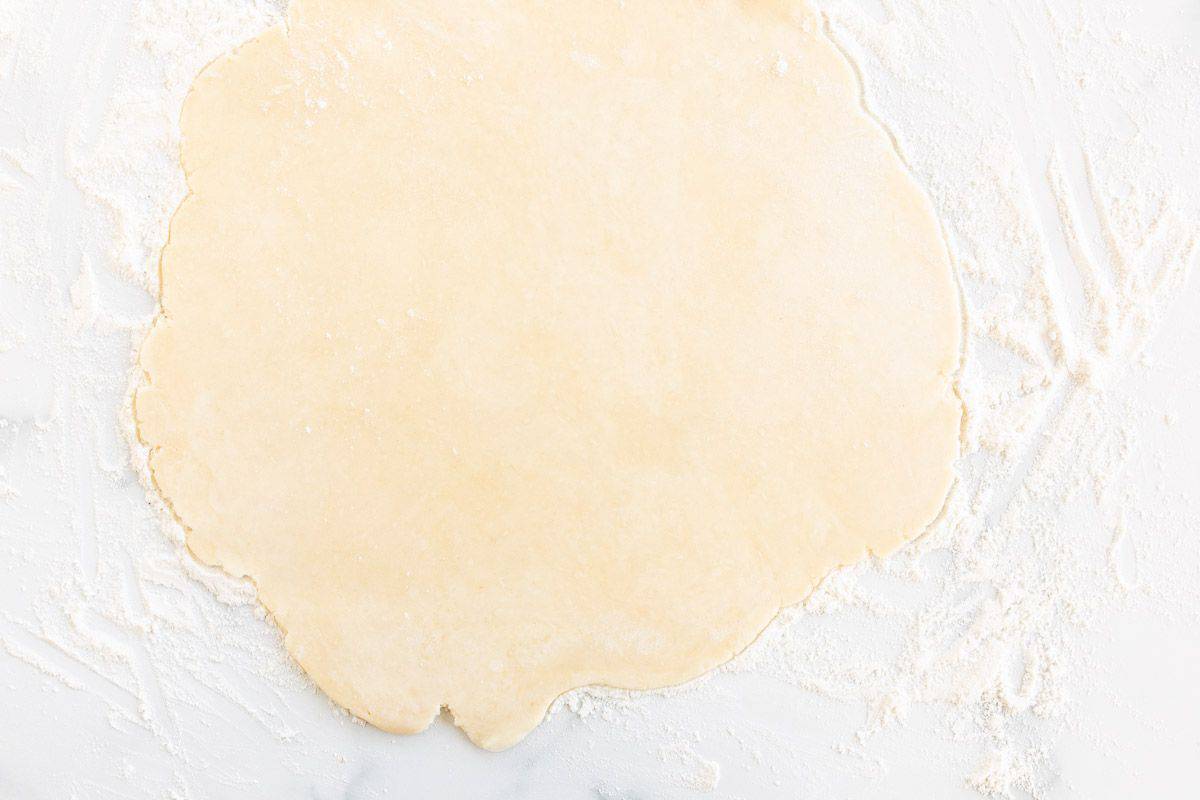 A homemade quiche crust rolled out on a marble surface