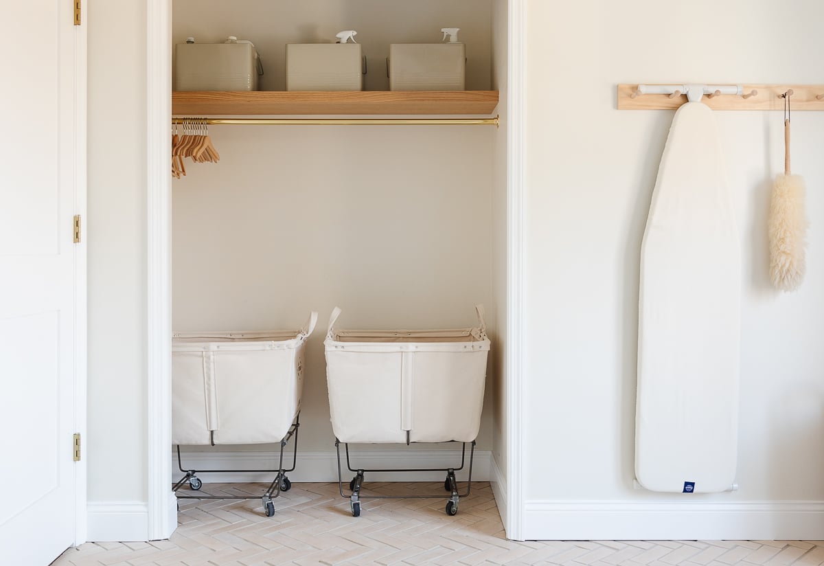 An organized laundry room with two baskets and an ironing board.